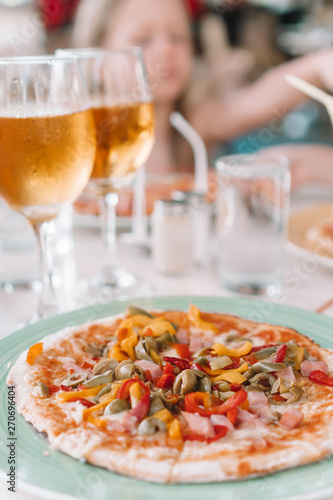 Pizza with mozzarella cheese, olive, fresh tomato and pesto sauce. Served at restaurant table
