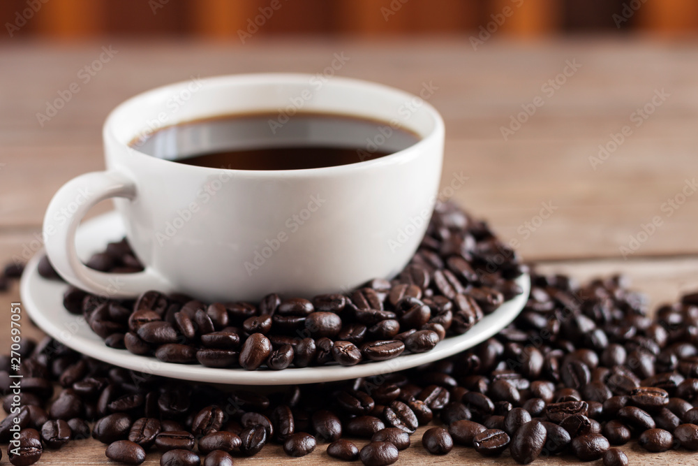 Coffee is hot, dark in a white coffee cup, placed on an old wooden table and has coffee beans - picture