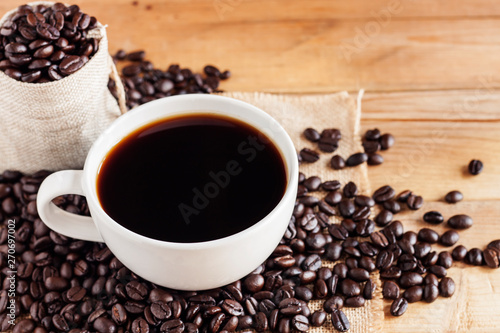 Hot coffee in a white coffee cup with sacks and coffee beans placed on old wooden tables and coffee beans - images