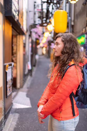 Tokyo, Japan Memory lane piss alley with yellow paper lamps lanterns background and young foreigner woman in Shinjuku area of city looking photo