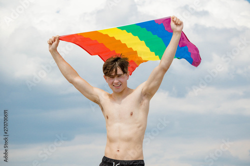Caucasian male on a beach holding a Pride flag
