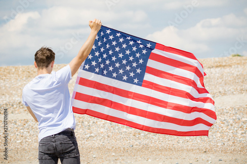 Caucasian male on a beach holding an American flag