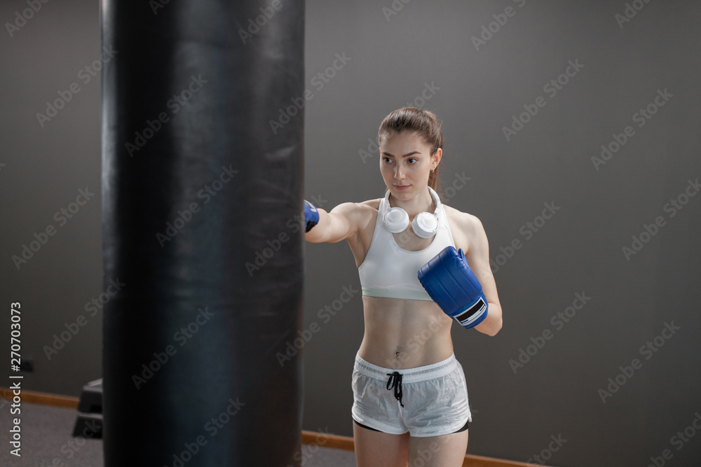 Young pretty woman in navy blue boxing gloves on a background of the gym.