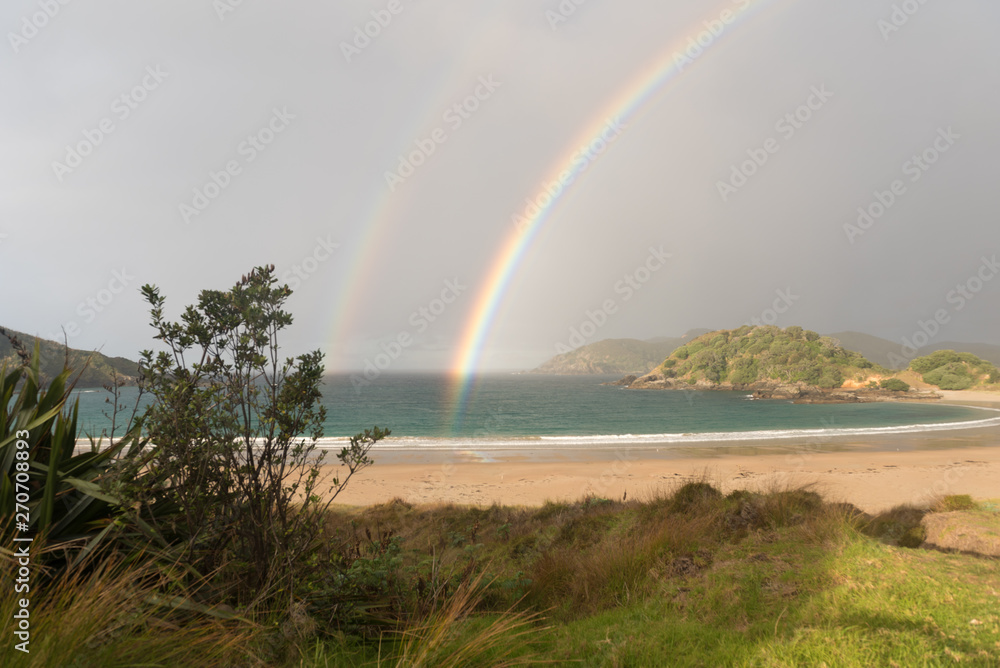 Φωτογραφία The end of a double rainbow over the deserted, sandy beach at Matai Bay with a small, silhouetted bush and flax in the foreground, Karikari Peninsula, Northland, New Zealand