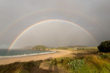 The complete arch of a double rainbow over the deserted, sandy beach at Matai Bay, Karikari Peninsula, Northland, New Zealand.
