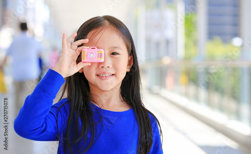 Adorable little Asian girl using a toy camera to take pictures outdoor. Kid development concept.