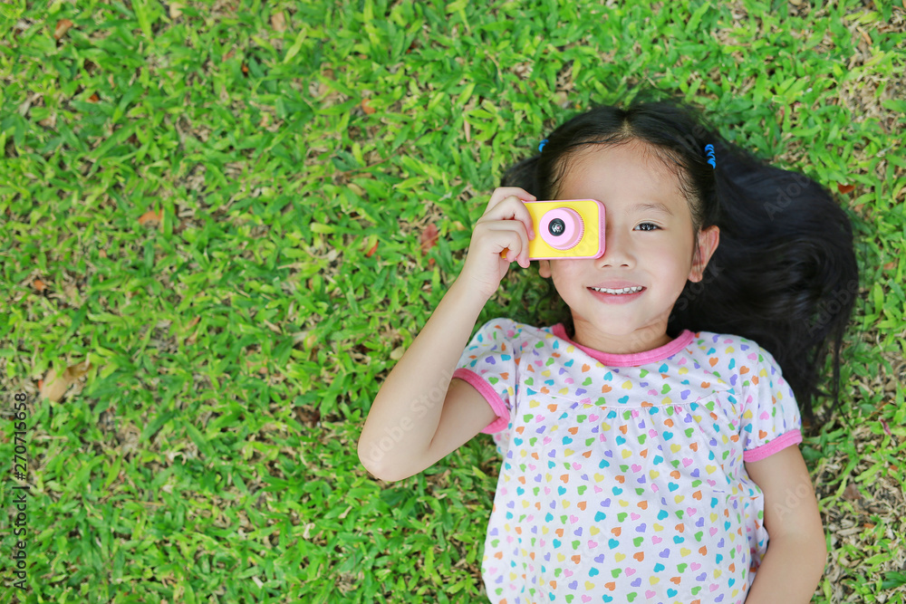 Happy little Asian child girl with digital camera lying on green lawn background. Happy little Asian child girl with digital camera lying on green lawn background.