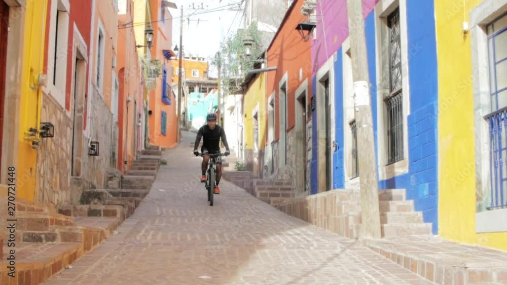 Hispanic man on a mountain bike descending from a colorful alley. Downhill cyclist on the streets of the city. Hispanic man on a mountain bike descending from a colorful alley. Downhill cyclist on the streets of the city.