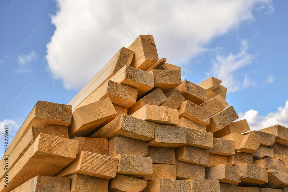 Stacked lumber on blue sky.Folded wood.Closeup wooden boards.The surface of the end of the board.Lots of planks stacked on top of each other in the warehouse.Lumber for use in construction. Stacked lumber on blue sky.Folded wood.Closeup wooden boards.The surface of the end of the board.Lots of planks stacked on top of each other in the warehouse.Lumber for use in construction.