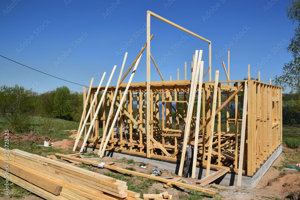 Construction home framing against blue sky.Wood frame residential building under construction.Building construction,wood framing structure at new property development site. mortgage, loan. Construction home framing against blue sky.Wood frame residential building under construction.Building construction,wood framing structure at new property development site. mortgage, loan.