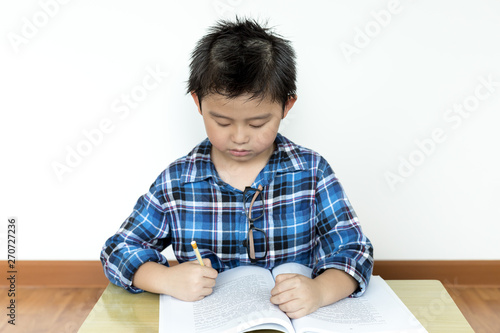 Little student boy without glasses doing his homework on the table with white background