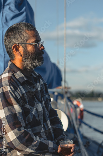 Weathered Man holding a Cocktail and looking Outwards on a Sailboat
