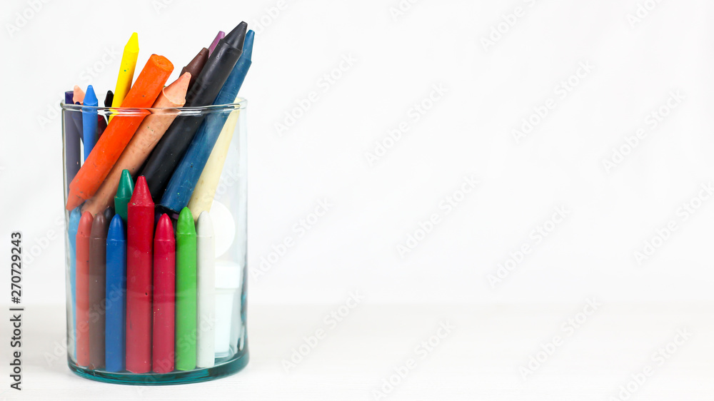 Fototapeta premium Many colourful crayon and School Supplies in glass bowl, isolated on a white surface.