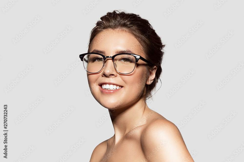 Portrait of beautiful smiling girl with bare shoulders posing in glasses. Pretty young brunette woman. Natural beauty and lifestyle concept. Isolated on grey background Portrait of beautiful smiling girl with bare shoulders posing in glasses. Pretty young brunette woman. Natural beauty and lifestyle concept. Isolated on grey background