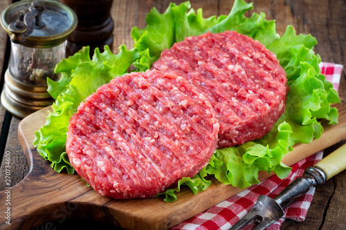 Raw mince meat beef burgers on a wooden cutting board with lettuce leaves