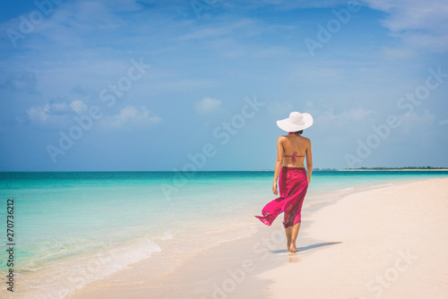 Luxury travel vacation elegant lady walking on beach in pink fashion skirt wrap relaxing on Caribbean holidays during winter. photo