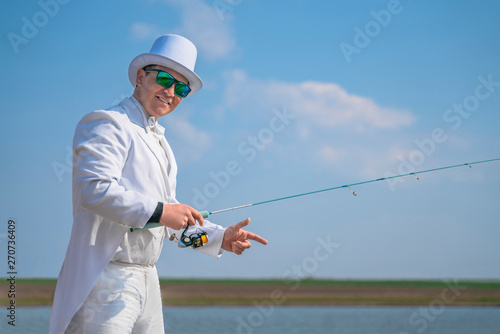 Exquisite fishing. Fisherman in white suit catch fish by spinning rod at lake