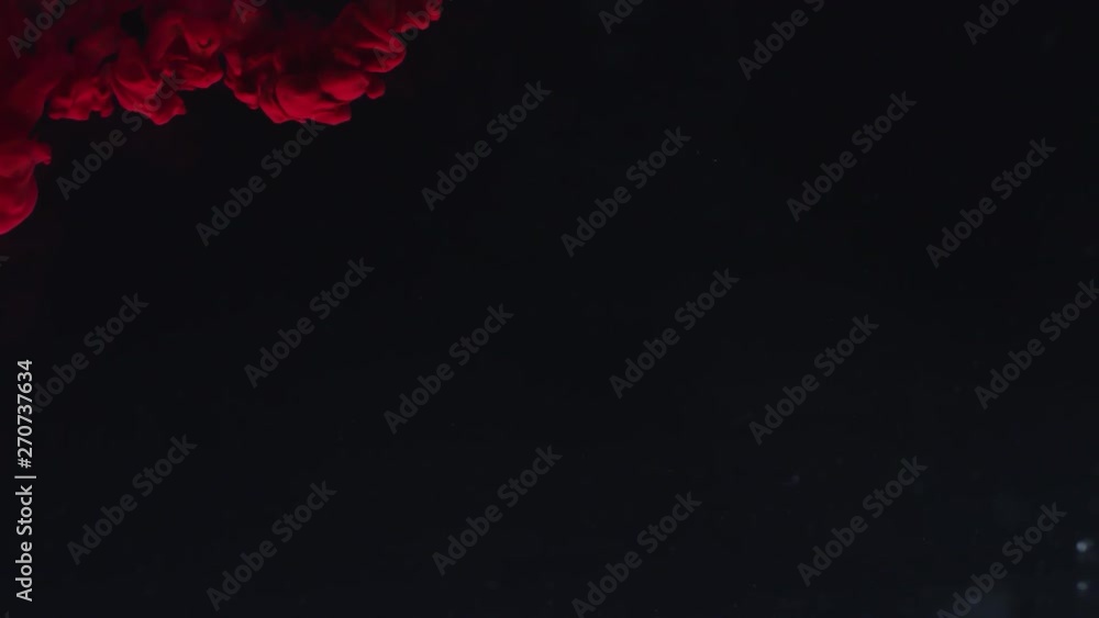 Slowmo shot with black background. Red paint drops falling in water and flowing creating abstract art Slowmo shot with black background. Red paint drops falling in water and flowing creating abstract art