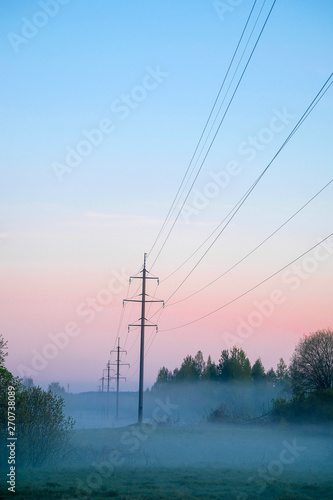 Power transmission line supporting structure at sunrise in the fog