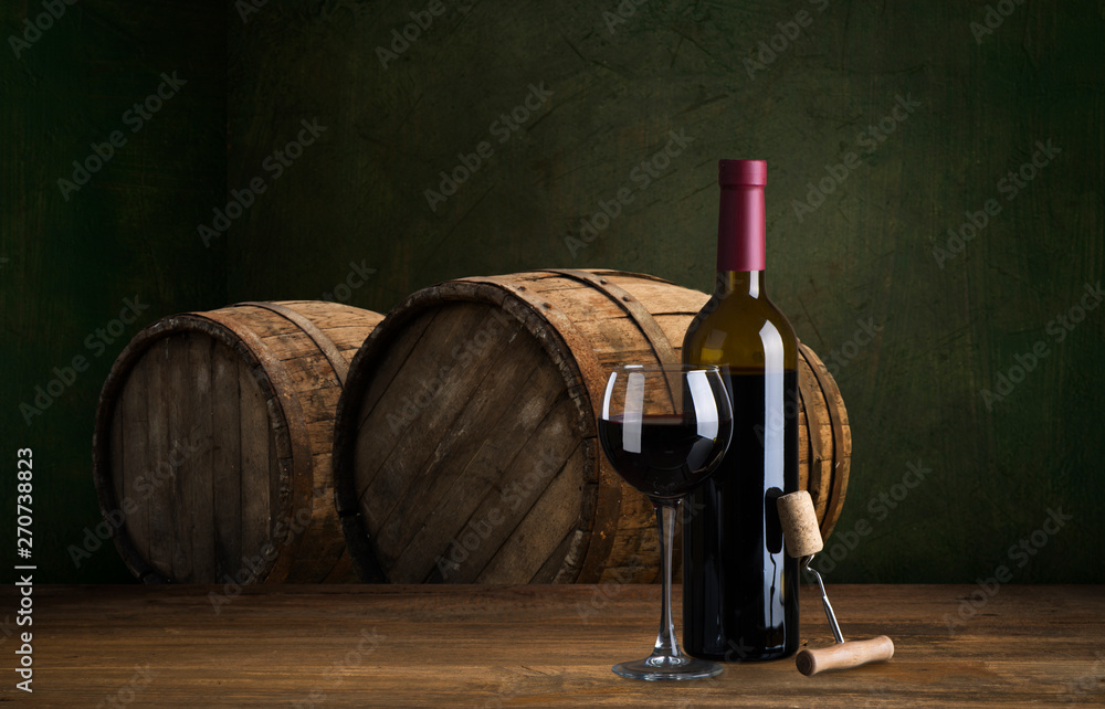 Bottle and glass of red wine on wooden barrel shot with dark wooden background