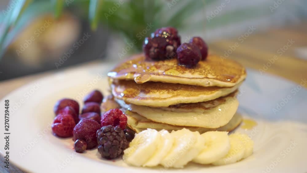 Stack of banana pancakes with fruits and pouring maple syrup Stack of banana pancakes with fruits and pouring maple syrup