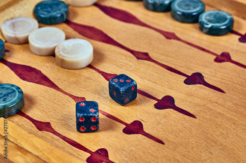 Backgammon game. Game dice made of stone lie on the backgammon board against the background of checkers. Close-up