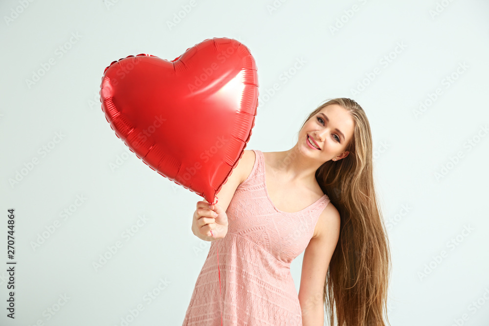 Beautiful young woman with heart-shaped air balloon on light background Beautiful young woman with heart-shaped air balloon on light background