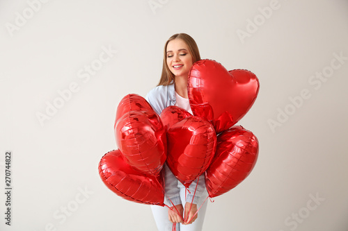 Beautiful young woman with heart-shaped air balloons on light background