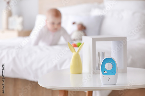 Modern baby monitor on table in room with little child
