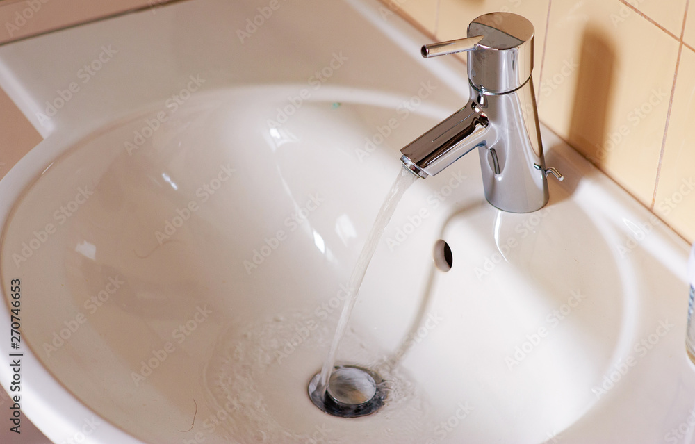 Water from the tap. A stream of clean water flows into the sink. Open chrome faucet washbasin. Warm tones. Water from the tap. A stream of clean water flows into the sink. Open chrome faucet washbasin. Warm tones.