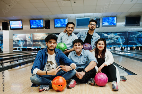 Group of five south asian peoples having rest and fun at bowling club, sitting on bowling alley with balls on hands.