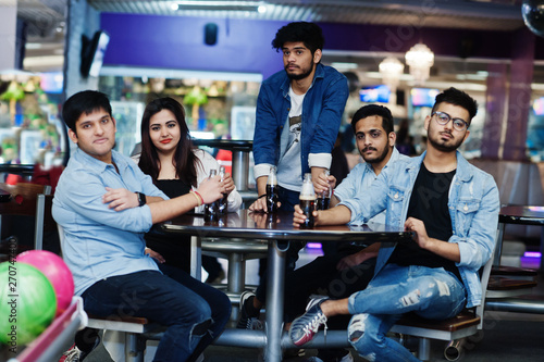 Fototapeta Naklejka Na Ścianę i Meble -  Group of five south asian peoples having rest and fun at bowling club, sitting on table and drinking soda drinks at glass bottles.