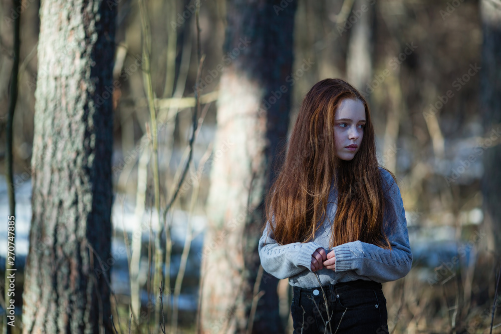 Long-haired thirteen-year-old skinny girl in a summer pine forest.