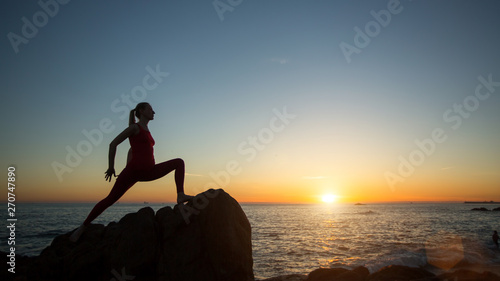 Fototapeta Naklejka Na Ścianę i Meble -  Silhouette of young woman doing fitness exercises on the beach at sunset.