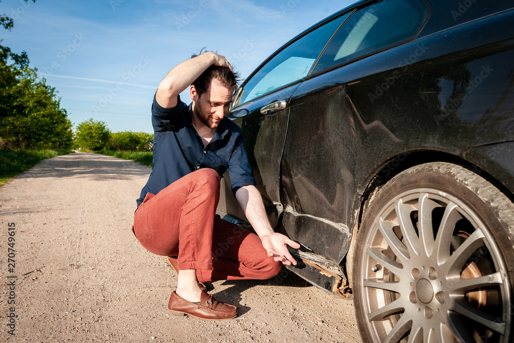 Angry man next to a car with damage on the left side and rotten sill on the bottom Angry man next to a car with damage on the left side and rotten sill on the bottom