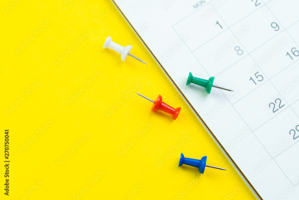 Flat lay or top view of clean white calendar with thumbtack or pushpin on vivid yellow background with copy space using as reminder, vacation plan, business organizer or meeting schedule concept Flat lay or top view of clean white calendar with thumbtack or pushpin on vivid yellow background with copy space using as reminder, vacation plan, business organizer or meeting schedule concept