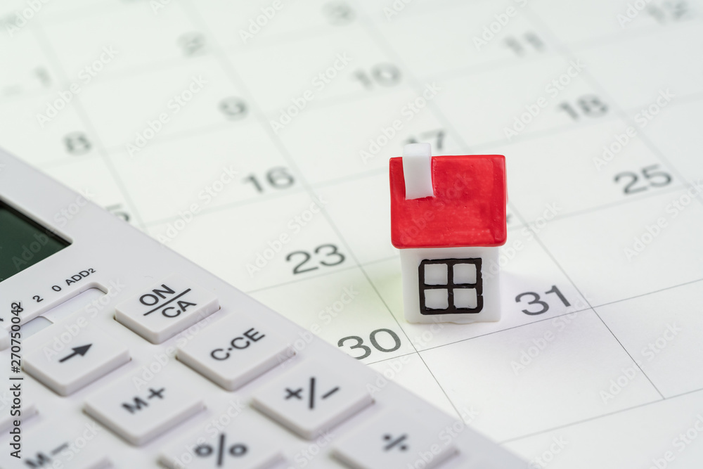 House mortgage payment and installment schedule concept, small miniature house on end of month calendar with calculator House mortgage payment and installment schedule concept, small miniature house on end of month calendar with calculator