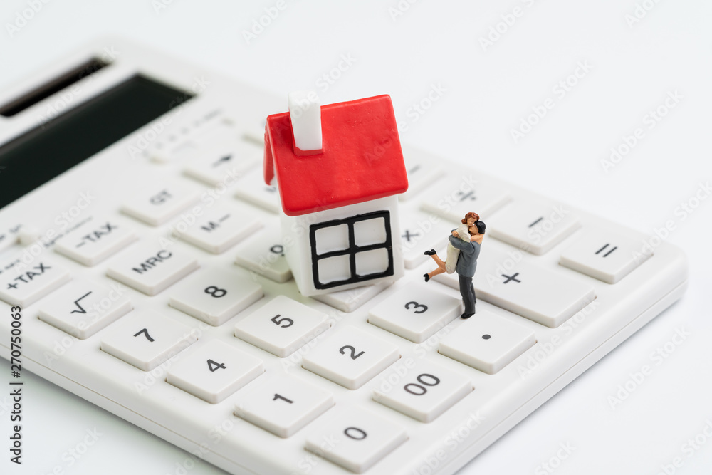 Family goals, building future with house cost calculation, mortgage and home loan or real estate concept, miniature couple figure with small house on white clean calculator on white background Family goals, building future with house cost calculation, mortgage and home loan or real estate concept, miniature couple figure with small house on white clean calculator on white background
