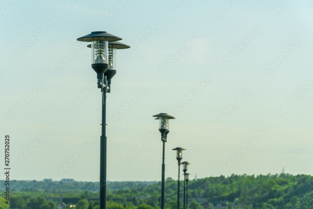 street lights in a row on the background of a light blue sky with haze and green trees