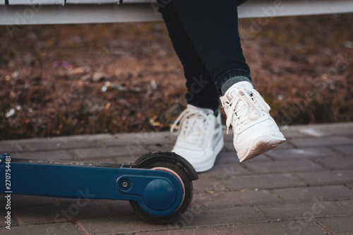 unisex legs in white sneakers next to the wheel of an electric scooter