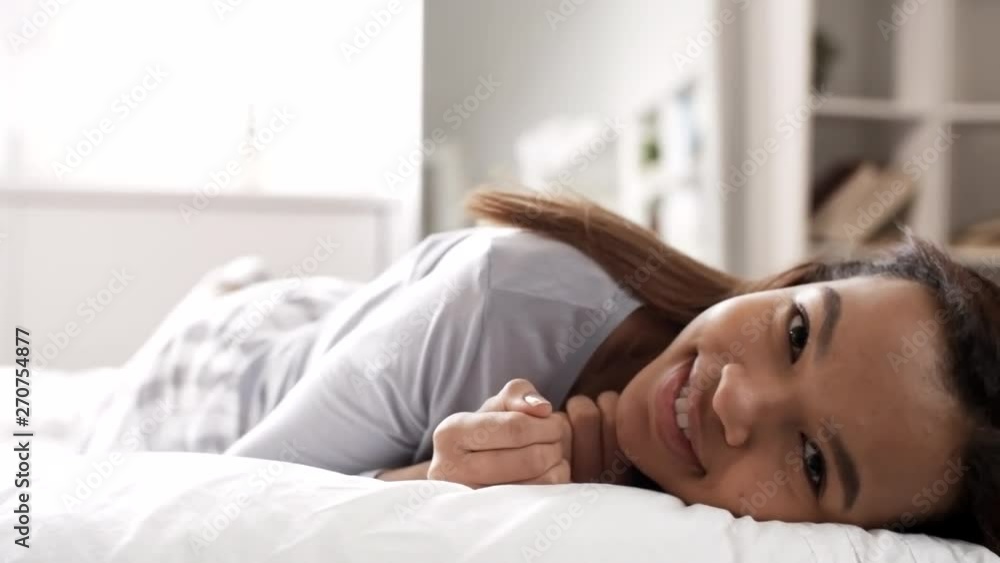 Young African woman in pajamas rolling over in bed and looking at camera with smile on her face Young African woman in pajamas rolling over in bed and looking at camera with smile on her face