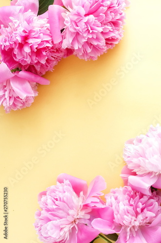 Bouquets of pink flowers peonies frame on pale yellow background. top view. copy space