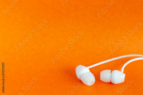 White earbuds on orange colorful background with copy space for text