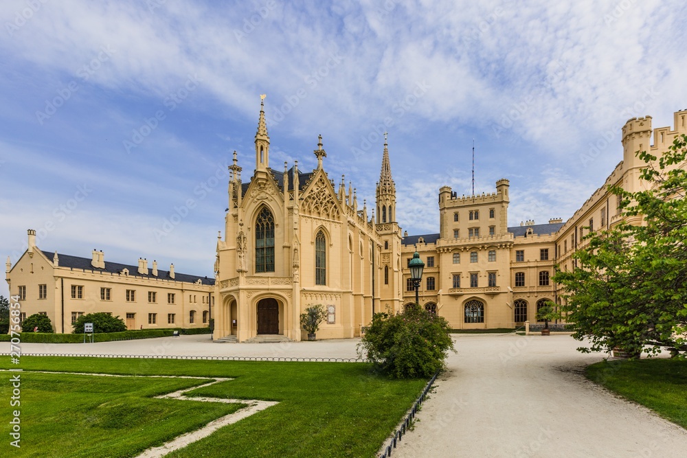 Lednice, Czech Republic - May 28 2019: Famous Lednice castle in South Moravia with yellow facade. Green lawn, trees and sand footpath in foreground. Sunny spring day, blue sky, white clouds.