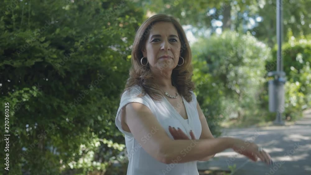 Elegant middle-aged woman in white blouse standing outside with crossed arms, changing body position, looking at camera, smiling, posing. Lifestyle concept Elegant middle-aged woman in white blouse standing outside with crossed arms, changing body position, looking at camera, smiling, posing. Lifestyle concept