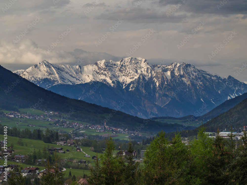 Spring mountain rural landscape. View over Stubaital Stubai Valley near Innsbruck, Austria with village Neder, green meadow, forest, snow covered alpen mountain peaks, evening dramatic clouds and
