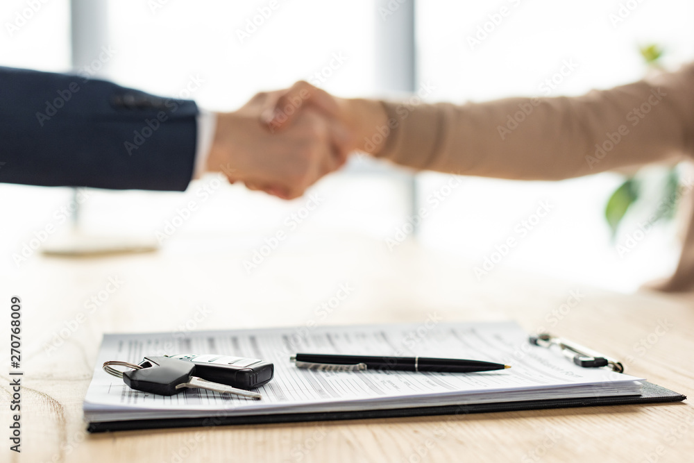 selective focus of clipboard, pen and car key near men shaking hands