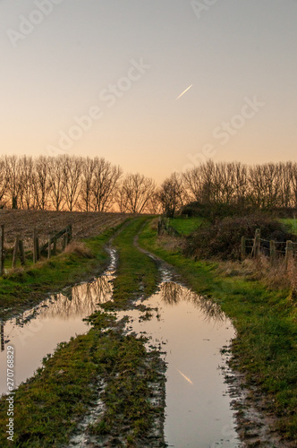 A contrail reflected in a trail running through a rural area in east flanders.