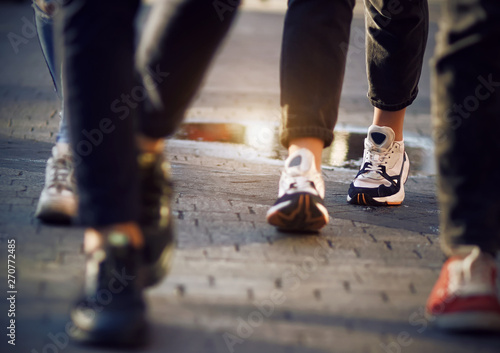 Women s feet in sports shoes among the crowd of passers-by who walk on the sidewalk after the rain  which is still puddles.