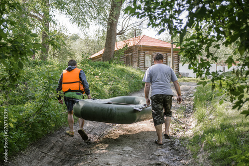 Adult man and a teenager together carry a rubber boat